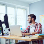 Creative smiling young man working on his start-up business in cozy home office