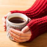 Hot mug of tea warming woman’s hands in retro jumper.