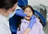 Dlaczego nie należy zwlekać z leczeniem zębów mlecznych u dzieci Dentystka w rękawiczkach bada zęby uśmiechniętej dziewczynki w gabinecie.