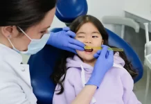 Dlaczego nie należy zwlekać z leczeniem zębów mlecznych u dzieci Dentystka w rękawiczkach bada zęby uśmiechniętej dziewczynki w gabinecie.