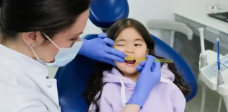 Dentystka w rękawiczkach bada zęby uśmiechniętej dziewczynki w gabinecie.