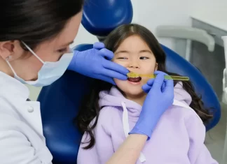Dentystka w rękawiczkach bada zęby uśmiechniętej dziewczynki w gabinecie.