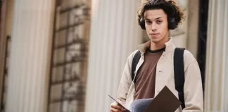 Student z teczką i słuchawkami przed budynkiem uniwersytetu.